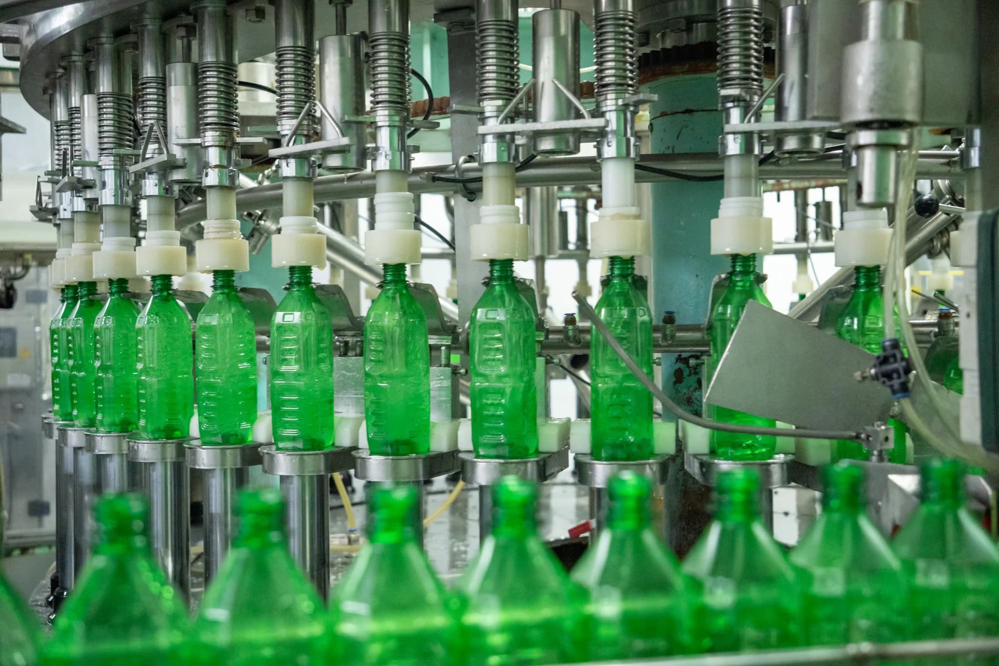 Green beverage bottles moving beneath filling nozzles on a production line.
