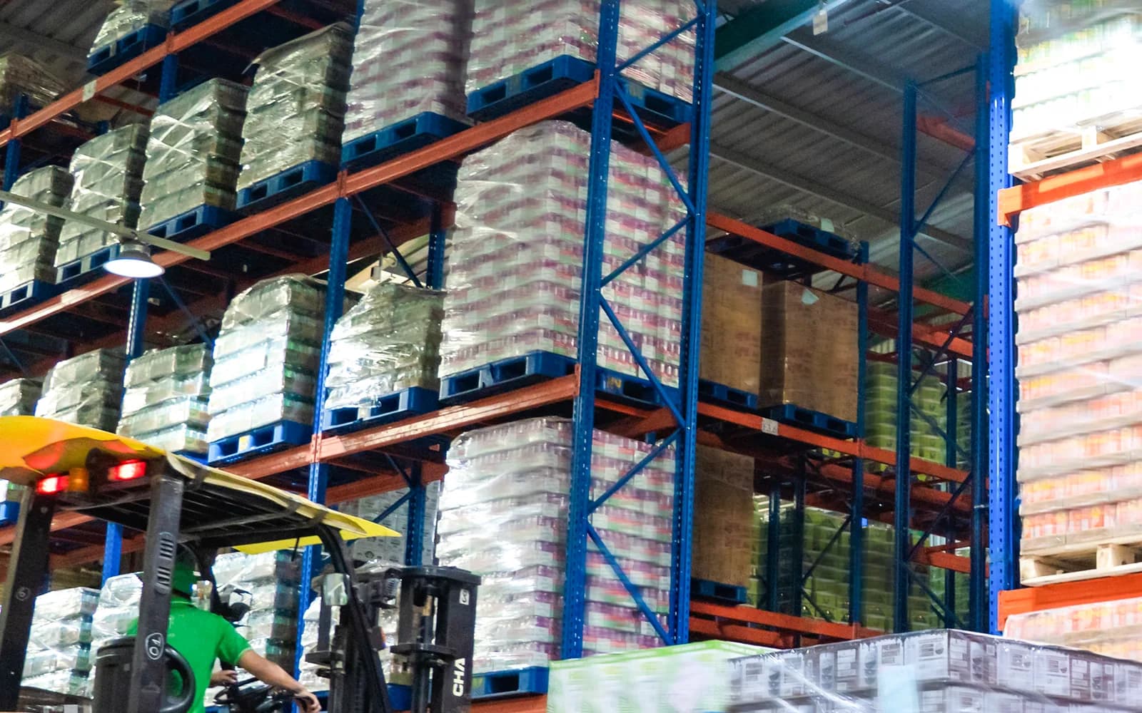 Palletized beverage cartons in warehouse racks with a forklift.