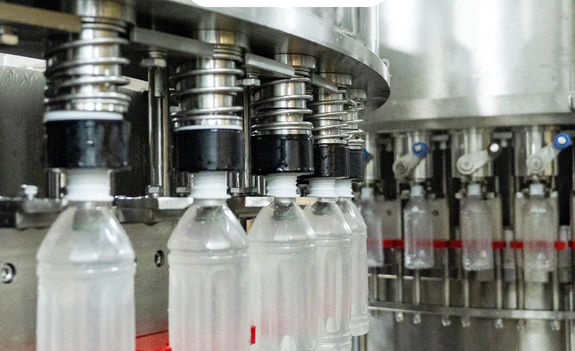 Des bouteilles de boisson transparentes avancent sur un équipement de remplissage.